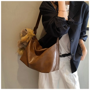 Détail du sac hobo en cuir marron avec large bandoulière et pendentif lion mignon
