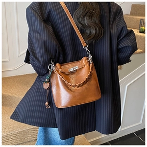 Detail of brown leather bucket bag featuring woven handle and silver metal swivel lock