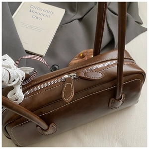 Détail d'un sac cylindrique marron avec surpiqûres blanches et un nœud en dentelle