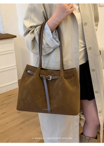 Detail of dark brown suede tote bag with slim straps and metal buckle shown in lifestyle scene