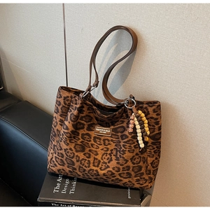 Detail of leopard print tote bag with brown leather handles and ethnic bead charm