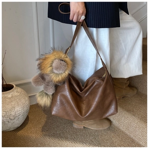 Détail du sac hobo en cuir marron avec un porte-clés lion en peluche et bandoulière large