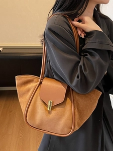 Brown suede and leather trapezoid bucket bag with gold buckle on a model in a black suit