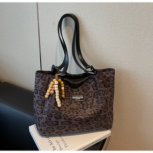 Detail of leopard print tote bag with black leather straps and colorful beaded charm