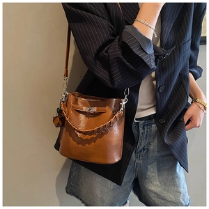 Detail of a brown bucket bag featuring a woven handle and metallic buckle in a lifestyle setting