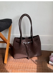Close-up of a dark brown suede tote bag featuring a retro buckle design and slim handles