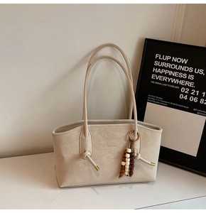 Detail of a beige leather tote bag featuring a textured finish and wood bead charm