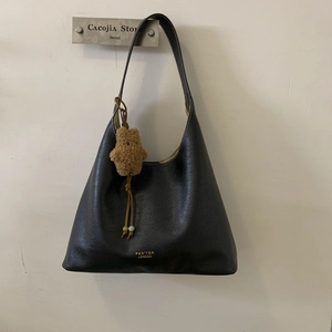 Detail of black leather hobo bag featuring gold brand logo and cute plush bear charm