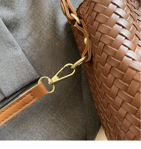 Detail of gold metal hook and woven leather texture on a brown bucket bag