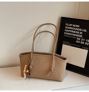 Detail of beige faux leather tote with golden logo and wooden bead tassel accessory