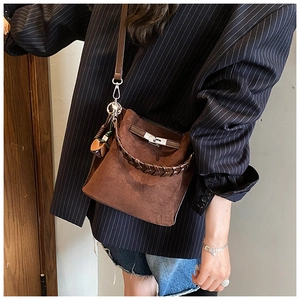 Close-up of brown suede bucket bag featuring woven handle and metal lock detail