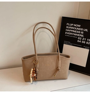 Detail of khaki tote bag featuring brand lettering and decorative wooden bead charm