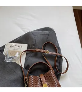 Detail of brown woven leather bucket bag with adjustable strap on white bedding
