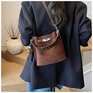 Detail of a brown suede bucket bag featuring a classic metal twist lock and woven handle