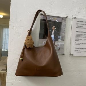 Detail of brown leather hobo bag with gold logo and plush bear charm hanging on the strap
