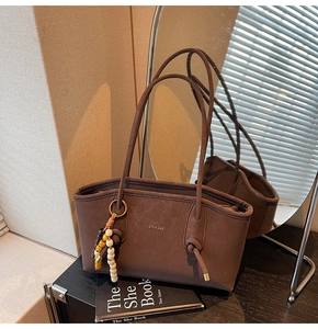 Detail of dark brown tote bag with smooth texture, gold lettering and beaded strap