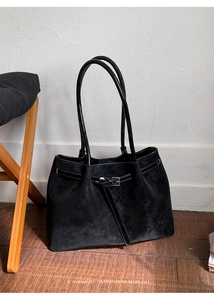 Close-up of black suede tote bag featuring decorative buckles and leather handles