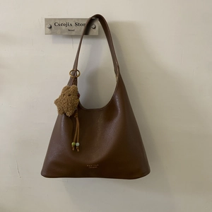 Detailed shot of brown leather hobo bag featuring gold brand logo and plush bear charm
