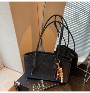 Detail of black vintage tote bag with metal logo and ethnic beaded tassel charm