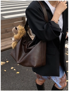 Détail d'un sac hobo en cuir marron foncé avec un ours en peluche sur un modèle street style