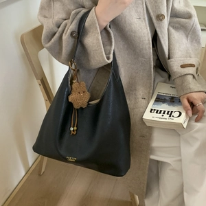 Chic black leather shoulder bag styled with an elegant beige coat and a cute bear charm