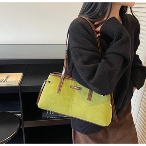 Detail of green suede shoulder bag with brown leather trim and metallic brand logo