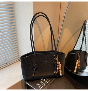 Close-up of black retro textured tote bag with gold logo and bohemian bead charm detail
