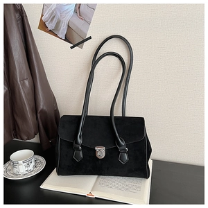 Detail of black suede shoulder bag on a book with lifestyle decor accessories