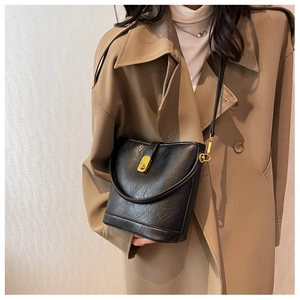 Close-up of a black textured bucket bag worn by a model in a classic khaki trench coat