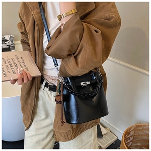 Detail of black bucket bag featuring metallic turn-lock closure and leather strap
