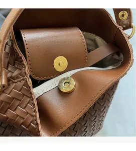 Detail of golden magnetic clasp and woven leather texture on a brown bucket bag
