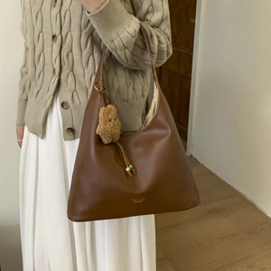 Detailed close-up of brown leather hobo bag with gold logo and cute teddy bear charm