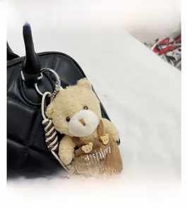 Detail of cute beige plush bear charm with fashion embroidery on a black quilted leather bag