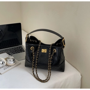 Detail der schwarzen gesteppten Shopper-Tasche mit Goldkette auf modernem Schreibtisch
