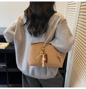 Detail of khaki leather shoulder bag with beaded charm accessory on model's shoulder