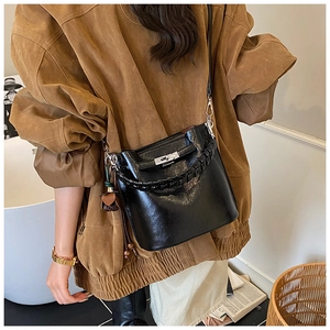 Detail of a black glossy leather bucket bag with silver twist lock and woven handle