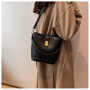 Detail of black faux leather bucket bag with gold metal twist lock on beige trench coat