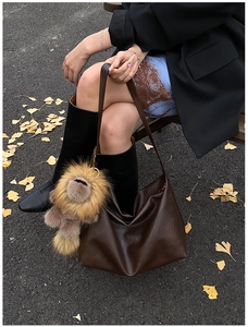Sac hobo en cuir souple marron foncé avec charm en peluche dans un décor de rue décontracté