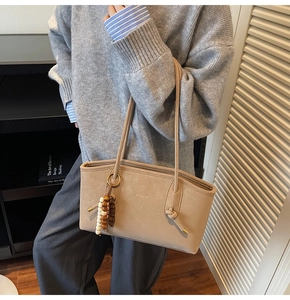 Detail of beige tote bag featuring knotted handle and decorative beaded accessory