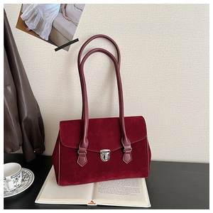 Detailed view of burgundy suede underarm bag with silver lock on vintage book background