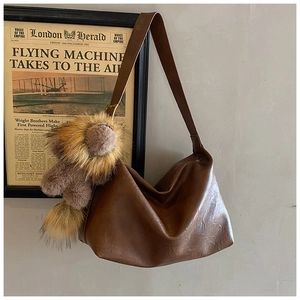 Gros plan du sac hobo en cuir PU marron avec un pendentif ours en peluche au mur