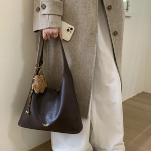 Detail of dark brown leather handbag with gold hardware and plush bear charm