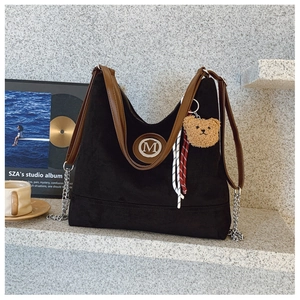 Détail du sac cabas en daim noir avec anses en cuir marron et breloque ours décorative
