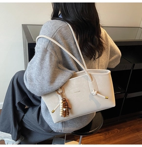 Close-up of cream tote bag featuring textured leather and decorative beaded tassel charm