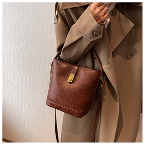Detail of a brown faux oil wax leather bucket bag featuring a gold metal clasp and strap
