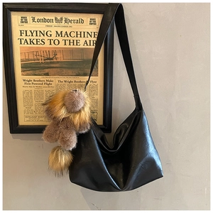 Détail du sac bandoulière noir en similicuir avec un charm décoratif en peluche marron
