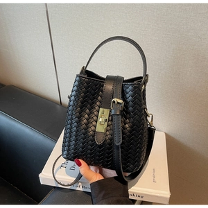 Detail of black woven leather bucket bag featuring a gold metal turn-lock and texture