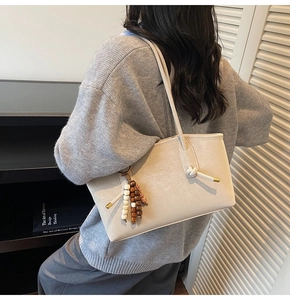 Detail view of beige leather tote bag featuring a knotted strap and colorful tassel charm