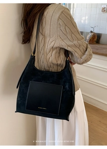 Detail of minimalist black suede and leather bucket bag featuring gold lettering logo