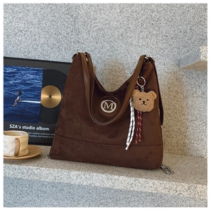 Détail du sac cabas en daim marron avec logo M en métal et breloque ours en peluche